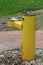 Back view of public park old dilapidated yellow two level drinking fountain for adults and children surrounded with gravel and