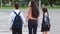 Back view responsible mother woman holds hands children son and daughter leads schoolchildren with backpacks to school