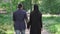 Back view of romantic muslim couple walking in park and talking. Camera follows loving bearded man in suit and young