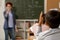 Back view of schoolboy raising hand to answer question of teacher