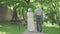 Back view of senior Caucasian couple walking in sunlight along the alley in summer park. Wide shot of loving old husband