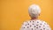 Back view of a senior gray haired woman isolated on the orange background