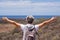 Back view of senior woman traveler enjoying outdoors trekking, looking at horizon over sea with open arms