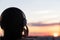 Back view silhouette of relaxed woman wearing headphones meditating listening to music on the beach at sunset.