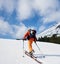 Back view of ski mountaineer walking up along snowy ridge with the skis in the backpack.