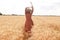 Back view of slender young lady rising her arms up to Sun, having walk in wheat field, wearing striped dress and straw hat, being