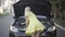 Back view of slim blond Caucasian woman in yellow dress checking open car hood on sunny summer road. Young lady driver