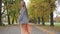 Back view of a slim Caucasian woman in checkered jacket and mustard dress walking in the autumn park. Young girl