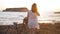 Back view slim young woman in headphones walking to bike on Mediterranean sea beach dancing in sunrays. Happy confident