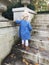 Back view of small blonde girl walking up cement steps in urban garden