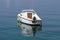 Back view of small white boat with outboard boat motor anchored in local harbor surrounded with calm clear blue sea