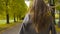 Back view of a smiling Caucasian woman in checkered jacket walking along the road. Young brunette girl strolling in the