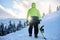 Back view of snowboarder climbing with his board on the mount for backcountry freeride session in the forest on sunset