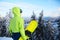 Back view of snowboarder standing with his board on the mount before backcountry freeride session in the forest. Man