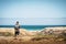 Back view of standing backpacker man looking at the beach and coast with blue sea and sky in background - concept of alternative