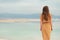 Back view of stylish girl wearing dress on seaside, Dead Sea beach. Travel, summer vacation, holiday, freedom concept. Digital