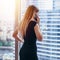 Back view of successful businesswoman having phone conversation looking out the window with cityscape view