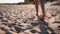 Back view of tanned woman legs and feet walking on sandy beach to the sea on sunny day. Slim pretty girl goes by the sea