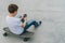 Back view.Teenager sits on skateboard,uses smartphone,digital gadget, plays computer games, browsing internet, chatting.