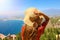 Back view of tourist woman with hat enjoying sicilian landscape view from Taormina town in Sicily, Italy