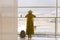 Back view of traveling girl standing near window at international airport terminal with backpacker on the floor