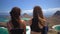 Back view two girls sitting on the top of hill and enjoying the water scenery of ocean and islands