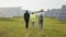 Back view of two inspectors in white helmets walking on solar station with technician in uniform. Multiracial engineers