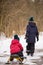 Back view on two siblings walking in a winter park. Children outdoors. Brother pulling sled with a toddler boy