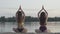 Back view of two slim women sitting in lotus pose on river bank. Confident female Caucasian yogi enjoying sunset