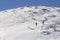 Back view of two tourist hikers with backpacks and hiking poles ascending snowy mountain slope on sunny winter day on white snow