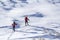 Back view of two tourist hikers with backpacks and hiking poles ascending snowy mountain slope on sunny winter day on white snow