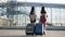 Back view of two young asian brunettes with long hair with their suitcases near the airport building
