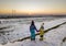 Back view of two young children in warm clothing standing in frozen snow field holding hands on copy space background of setting