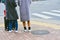 Back view of two young tourist women with luggage standing on sidewalk at the junction waiting for a signal to cross the road