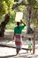 Back view of unidentified woman collecting water in large container and carried balanced on head