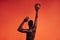 Back view of unrecognizable African American male athlete throwing basket ball against an orange background