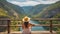 Back view of unrecognizable young female traveler in straw hat sitting on wooden pillar admiring breathtaking scenery of river