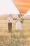 The back view of the vintage dressed newlyweds walking in the field near the airballoon.
