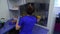 Back view of the woman in blue uniform and rubber gloves putting the rack for test tubes in the special fridge