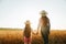 back view, woman and daughter child with hat on head examines farmland,