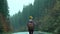 back view woman hitchhiker traveler with backpack walks alog road outdoors in cold wet foggy autumn day and waites a car