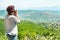 Back view of a woman photographer taking pictures of the valley with mountains from above.