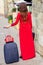 Back view of woman in red dress pulls suitcase on road of city street