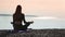 Back view woman sitting in lotus position on mat at sunset beach. Shot with RED camera in 4K