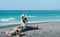 Back view of woman sitting on the trunk and looking to beautiful turquoise water at black sand beach of Napier town, New Zealand.