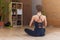 Back view of woman sitting in yoga lotus pose relaxing and meditating in living room
