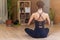 Back view of woman sitting in yoga lotus pose relaxing and meditating in living room