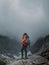 Back view of a woman standing on the top of a rock and enjoying the foggy nature on a gloomy day