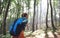 Back view woman traveler with big backpack hiking walking on rocky trail throught forest, sun rays shine through trees.