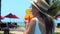 Back view of woman with tropical cocktail in her hands relax and chilled in swimming pool near sandy beach with palm